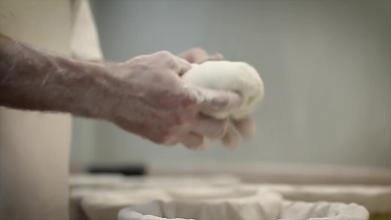 Flour-dusted hands gently shaping bread dough in an artisanal bakery.